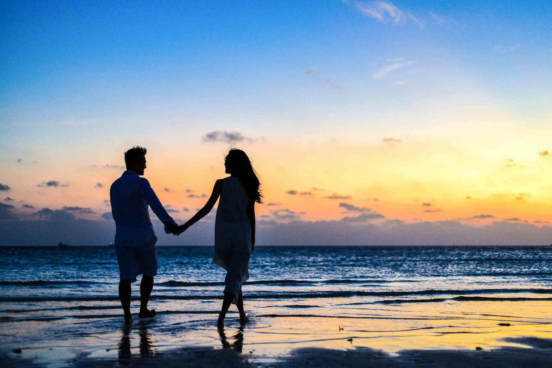 Mann Und Frau, Die Hände Gehen, Die Während Des Sonnenaufgangs An Der Küste Gehen